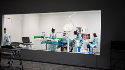 Hinter einer Glaswand operiert Wainwright mit seinem Team eine Patientin. Die Zuschauer können aus dem benachbarten Raum jederzeit Fragen stellen.