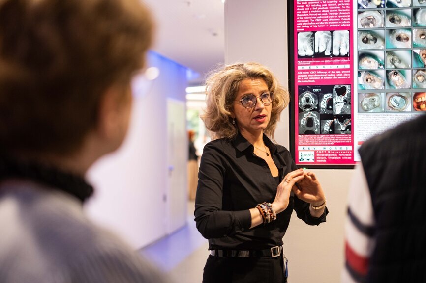 Attendees listen to a poster presentation. The posters are displayed on various screens across the venue.