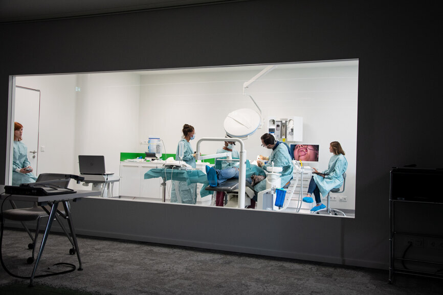 Hinter einer Glaswand operiert Wainwright mit seinem Team eine Patientin. Die Zuschauer können aus dem benachbarten Raum jederzeit Fragen stellen.