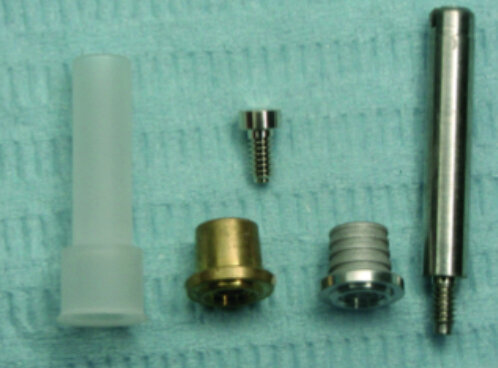Fig. 4 : Composants pour technique de collage (de gauche à droite) : Préforme calcinable, bague de centrage (laiton), bague de collage (titane), vis de fixation or M 1.4, vis de laboratoire. 