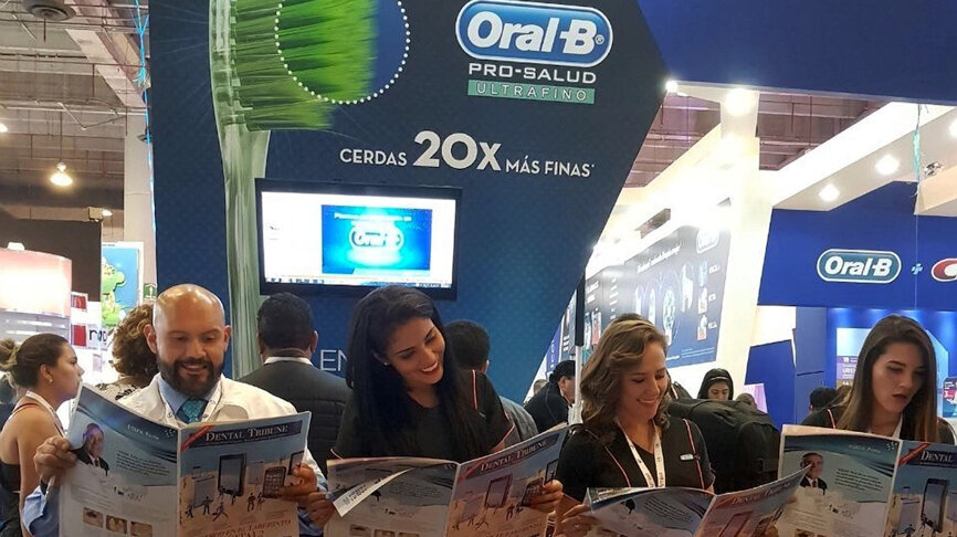 Un grupo de expertos de Oral-B lee Dental Tribune frente a su stand.